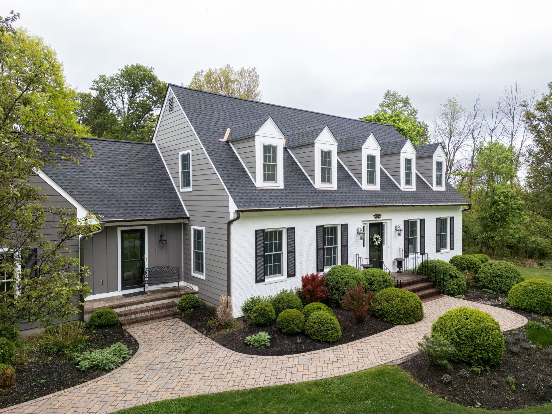 A white house with black shutters, gray siding, and a gray asphalt roof with five small gables.